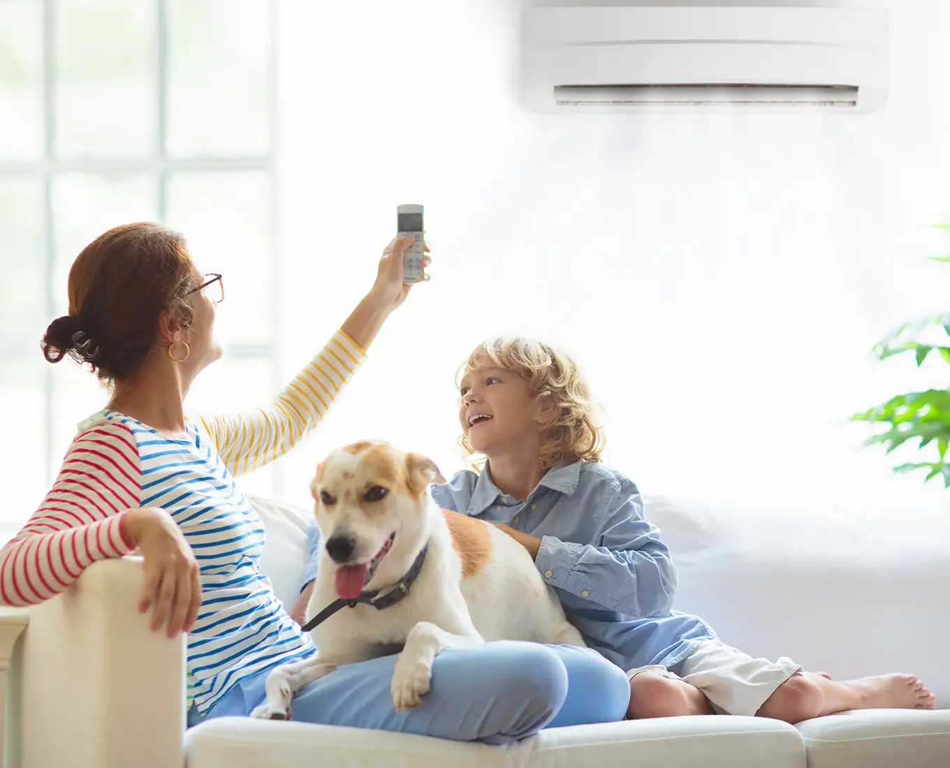 Mother adjusting the remote for a ductless air conditioning system while relaxing at home with her child and dog in Springfield, IL.