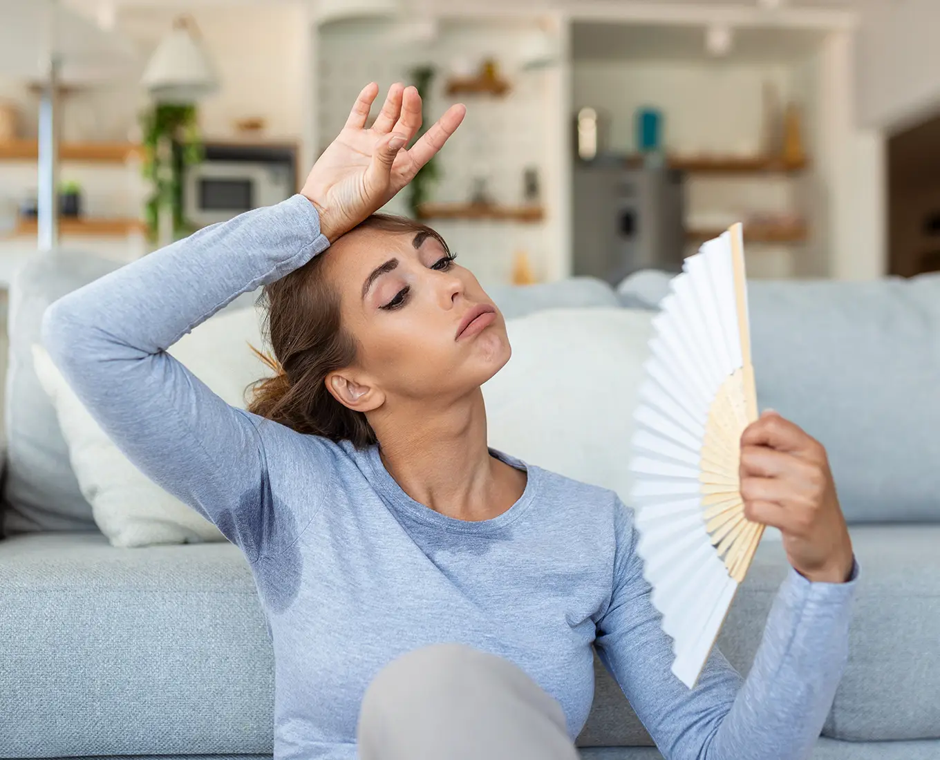 Homeowner feeling overheated and fanning herself while waiting for emergency AC repair service in Springfield, IL.
