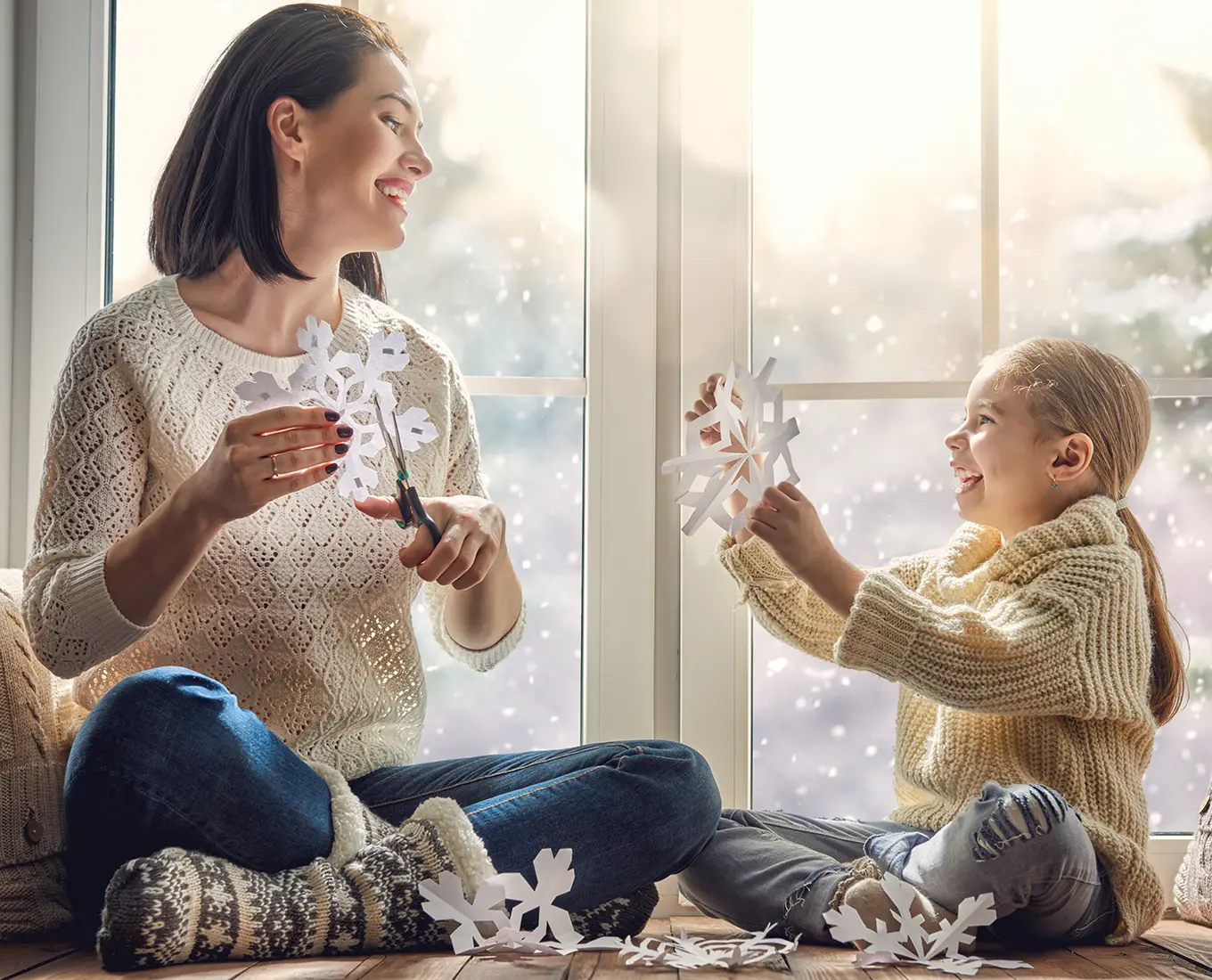 Mother and child making paper snowflakes by a sunny window while their home stays warm thanks to dependable furnace maintenance services in Springfield, IL.