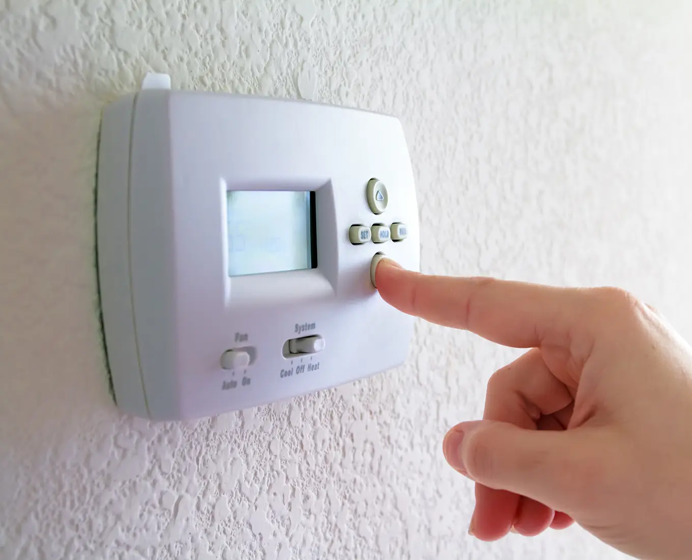 Hand adjusting a home thermostat to control indoor temperature after professional furnace maintenance service in Springfield, IL.